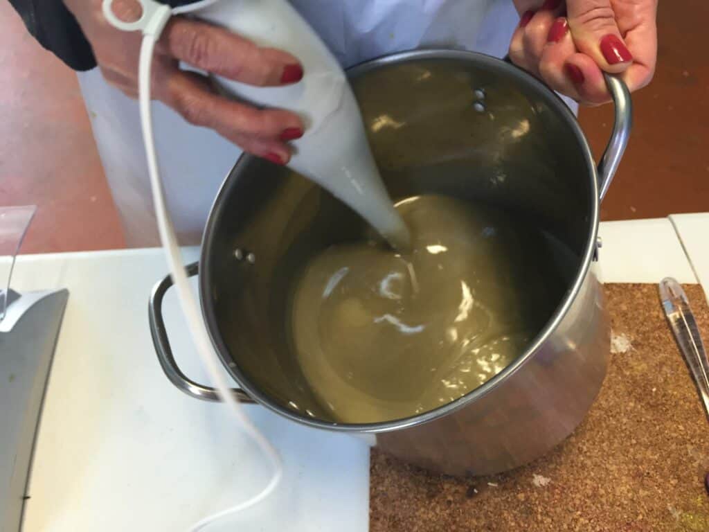 stick blending oils and sodium hydroxide solution in a stainless steel pot.