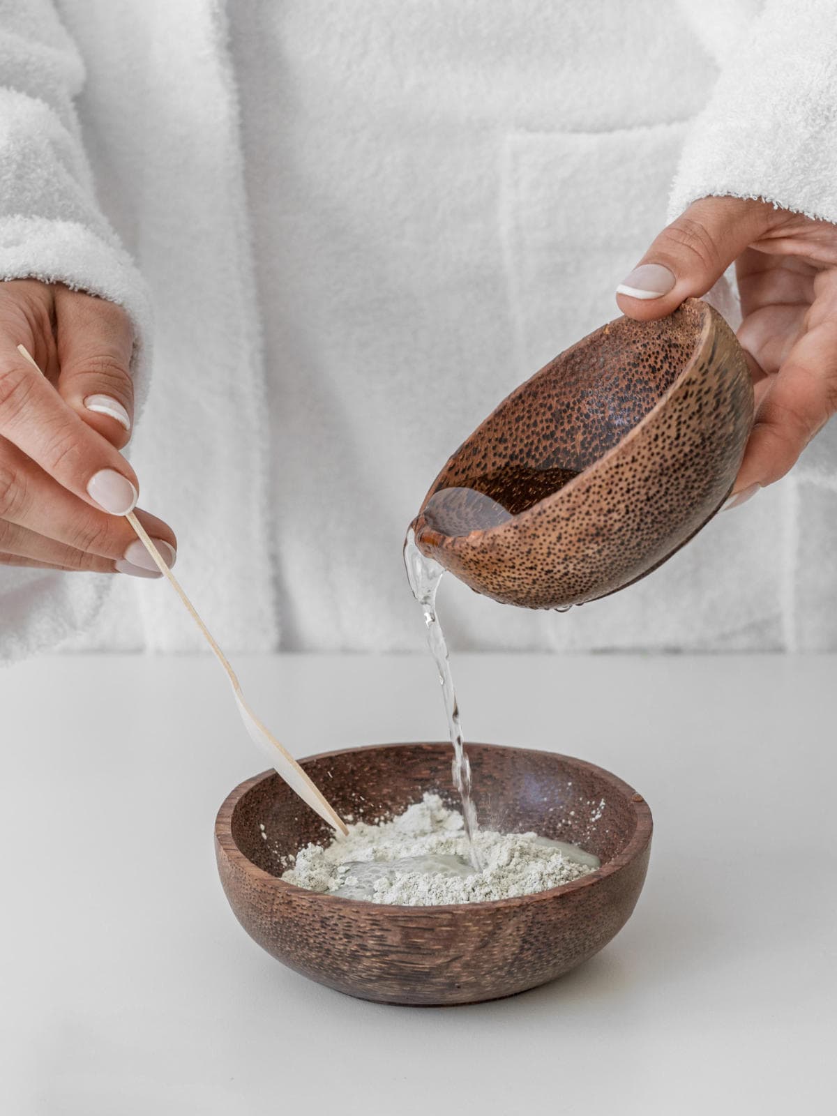 pouring a liquid into a bowl of powdered French green clay.