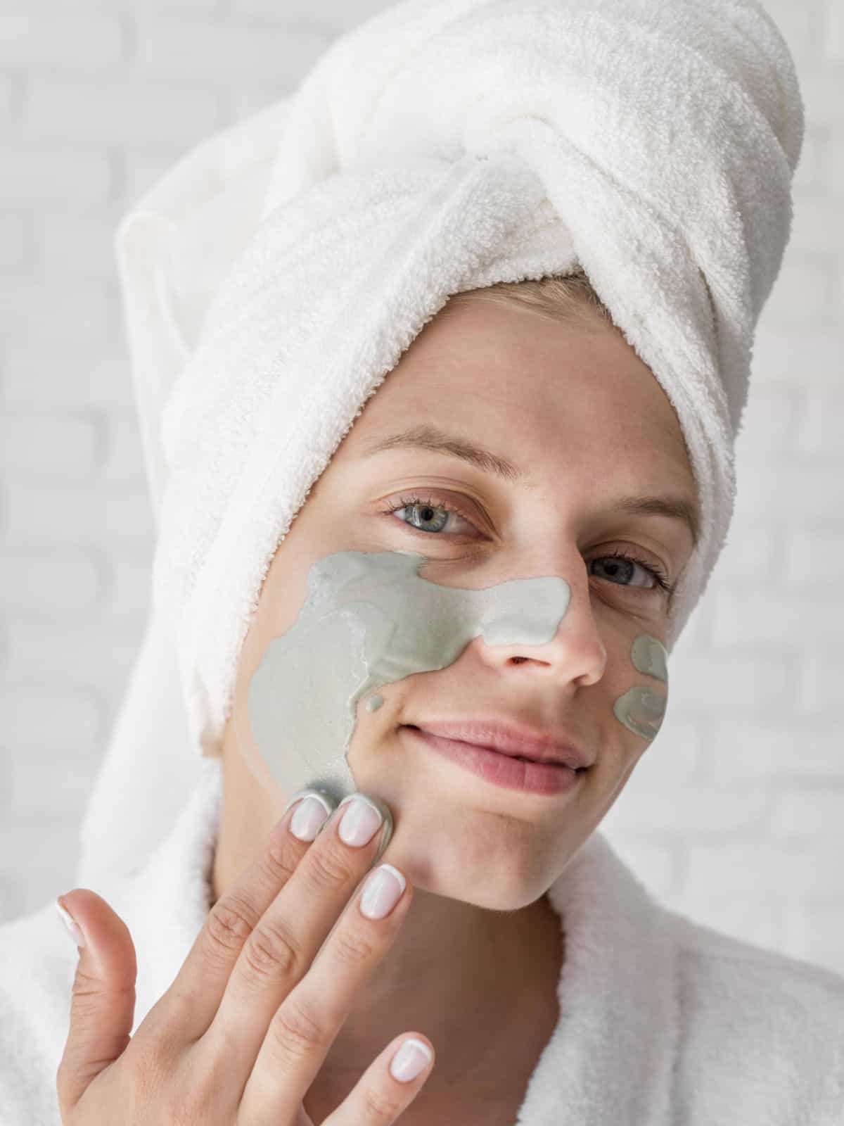 Woman using her fingers to coat wet French green clay mask on her face.