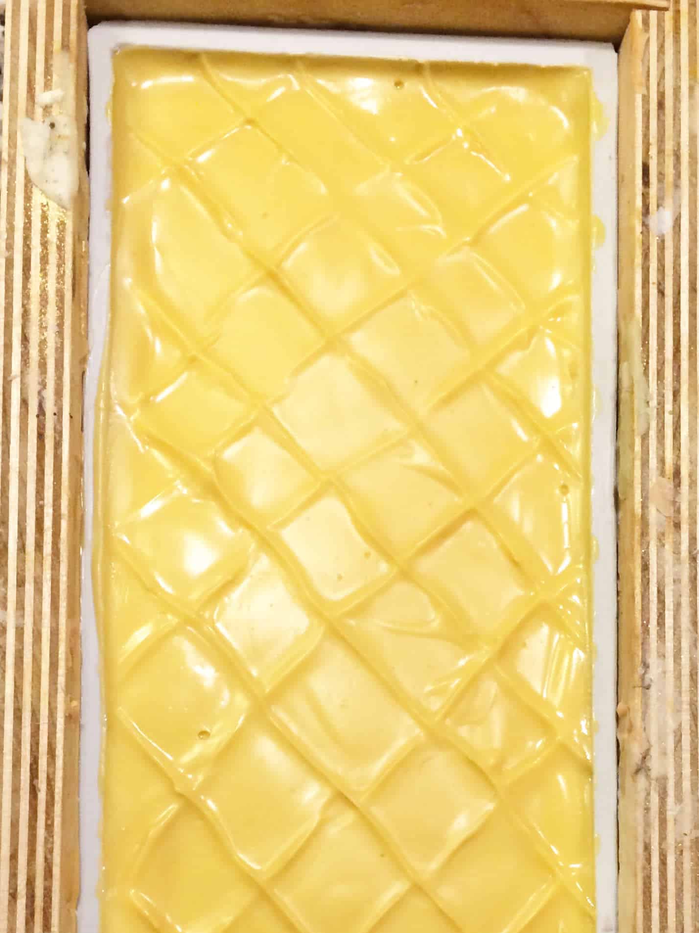 decorated cross hatch top of wet yellow clay soap in a log soap mold.